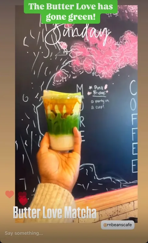 A hand holding the green Butter Love drink in front of the chalkboard
