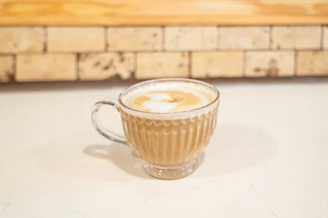 A hot latte in a glass mug against the brick counter